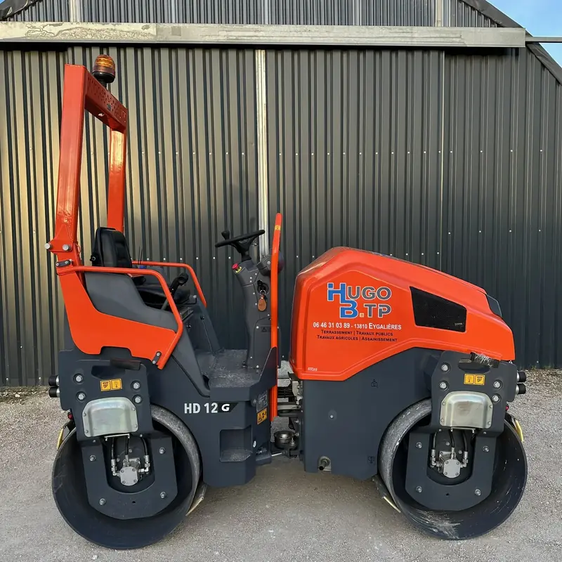 Rouleau compacteur HAMM HD12 orange du parc de location Hugo BTP, de profil